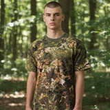 Ein junger Mann trägt ein id-paintball T-Shirt mit WASP Z3A Tarnmuster aus atmungsaktiver Baumwolle im Wald.