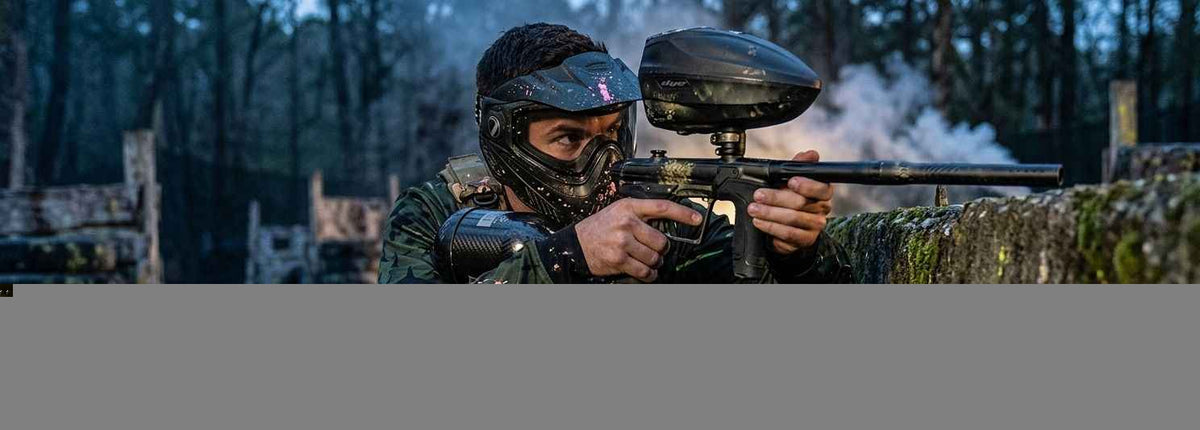 Paintballspieler mit Maske und Markierer beim Woodland-Paintball hinter einer Deckung.