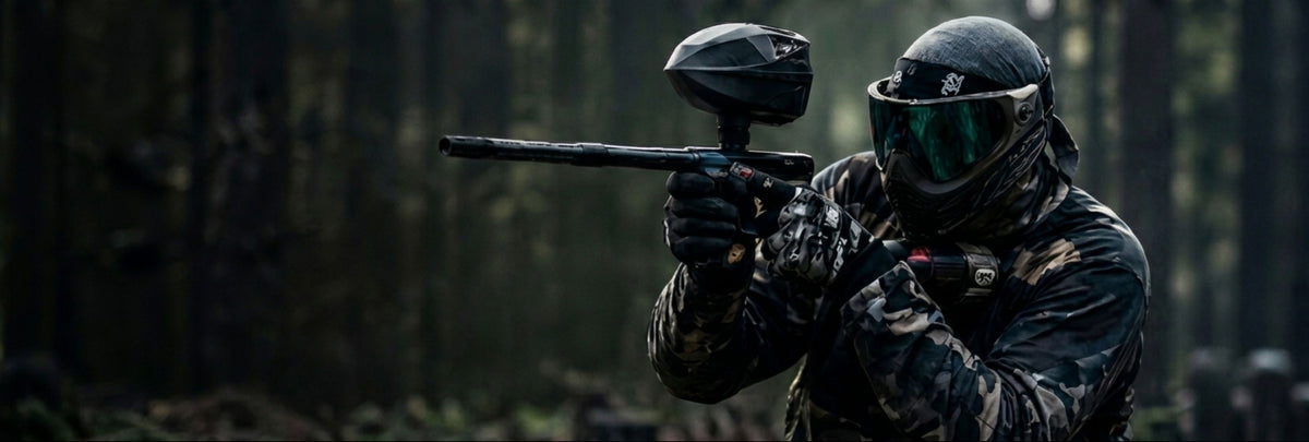 Paintballspieler im Camouflage-Outfit mit Paintball-Markierer und Maske beim Woodland Paintball im Wald.